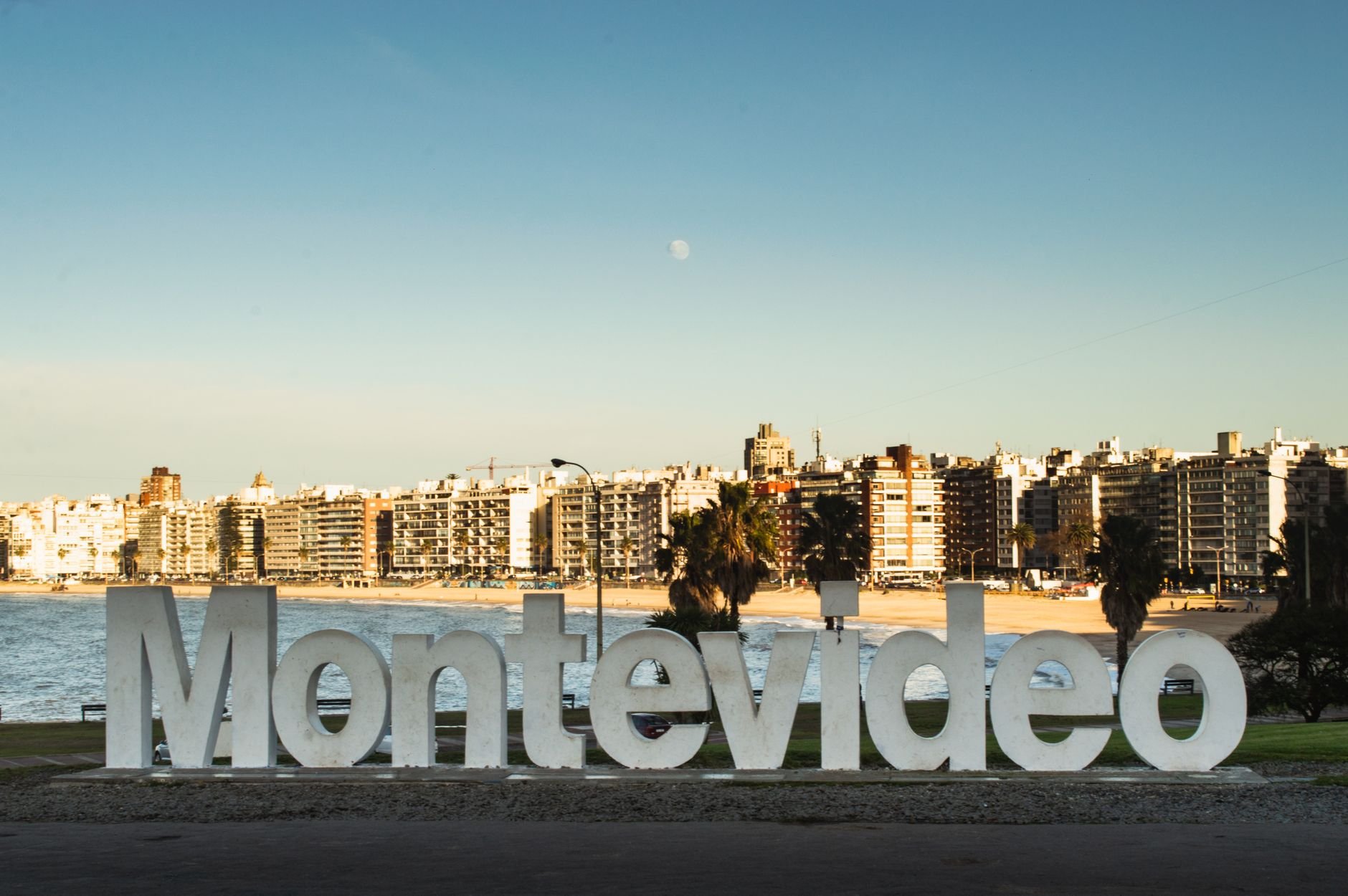 The illuminated city skyline at dusk, seen across a curving bay beneath a rising moon.