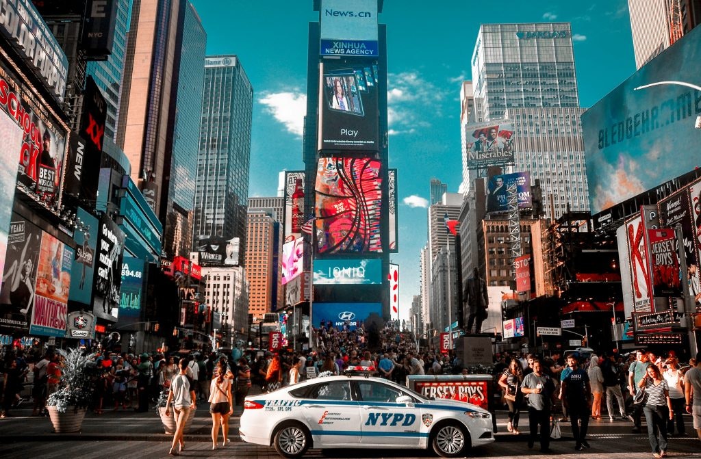 A New York City Police car and pedestrians can be seen under the bright lights of Times Square.