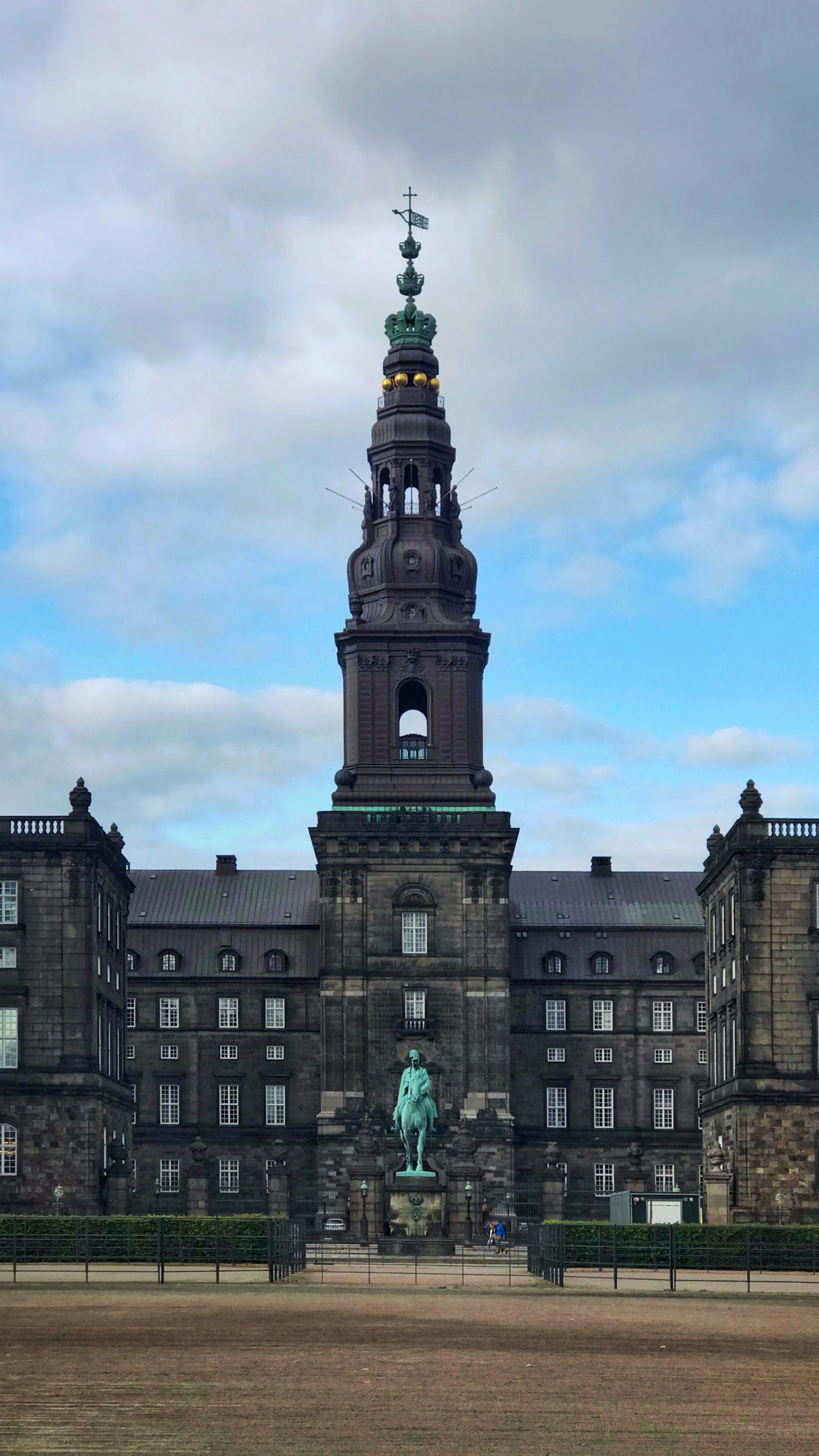 The tower of Christiansborg Palace rises over its riding-ground courtyard and equestrian statue under an overcast sky.