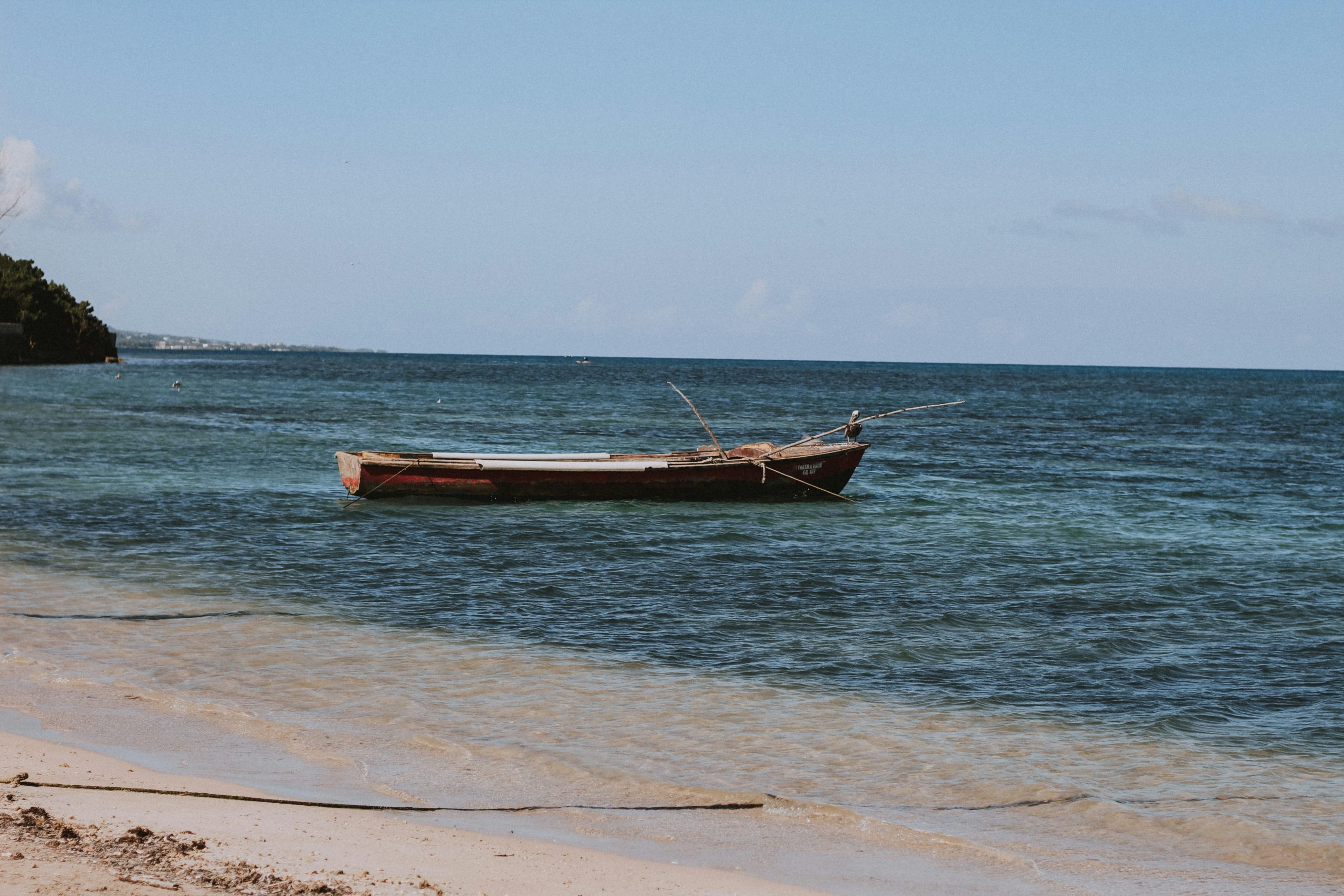 Wooden boat anchored near the shore of a calm beach in Jamaica with clear water.