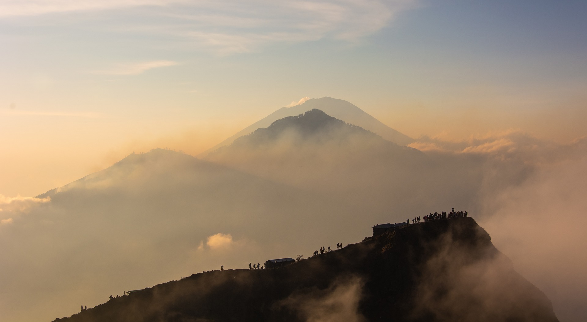 Hikers gather on a ridge overlooking Mount Batur's volcanic peak above a sea of clouds