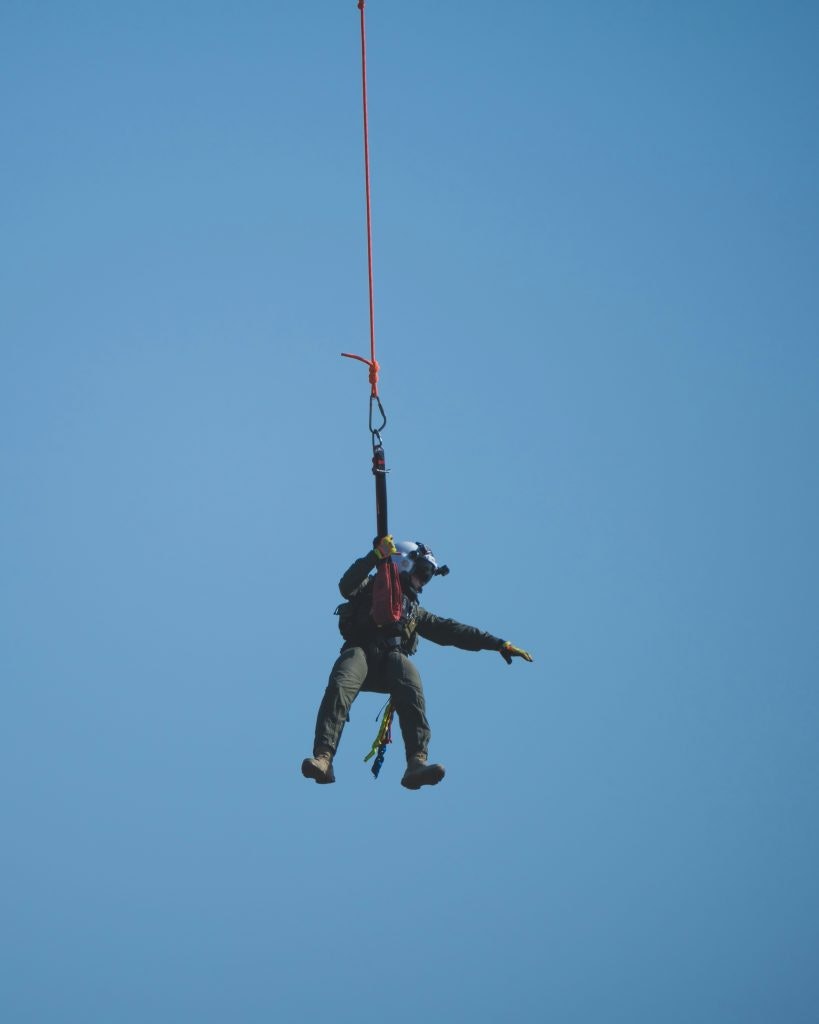 During a rescue operation a man is hanging from a rope in the air and directing the helicopter search.