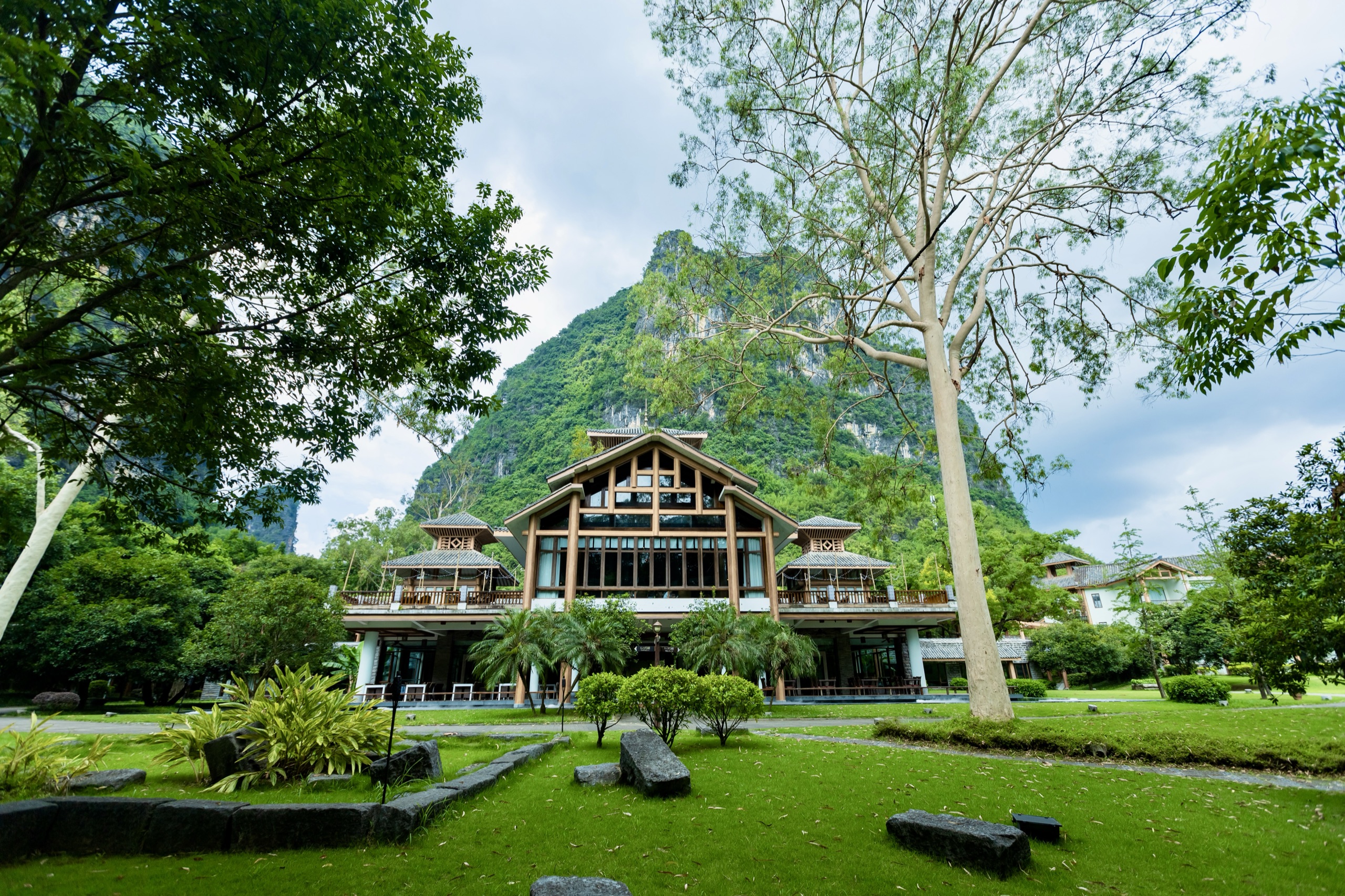 A timber lodge set in lawns below a forested limestone karst peak near Yangshuo, China