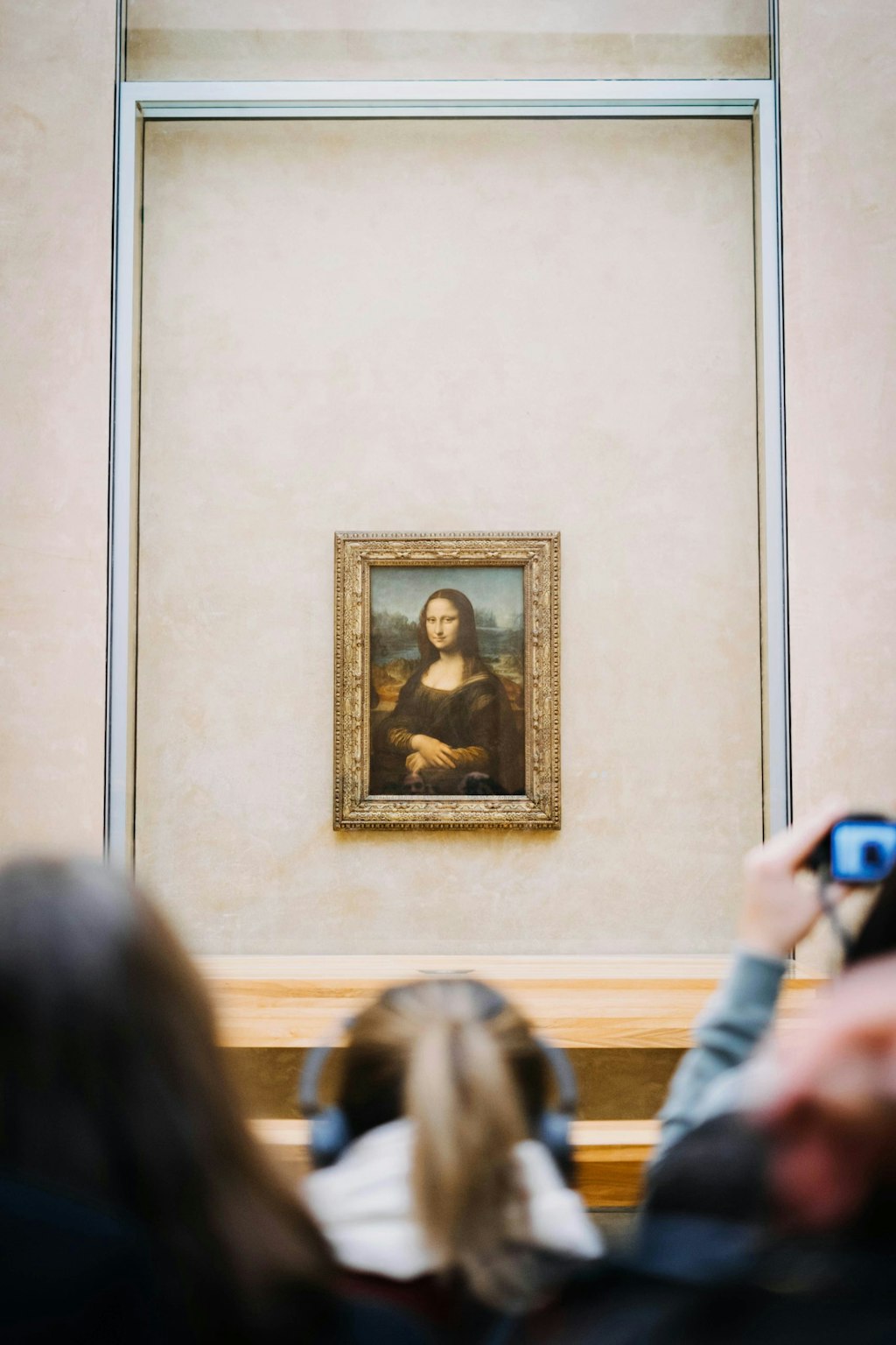 Crowds gather in front of the Mona Lisa, Leonardo da Vinci's iconic painting, displayed in a glass case at the Louvre.
