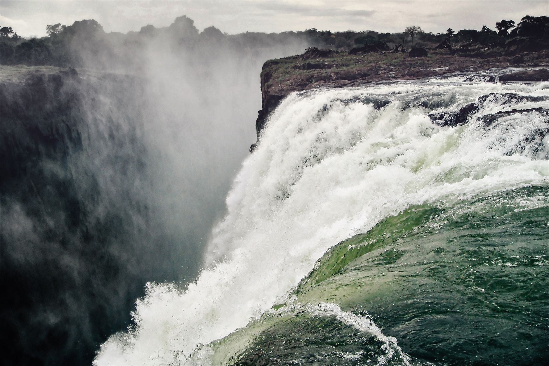 Victoria Falls seen from close to the lip, heavy white water pouring over the rock edge into the gorge.